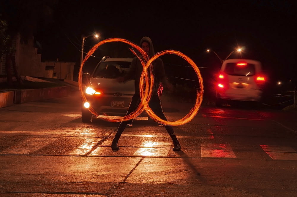 a man holding two fire hoopes in front of a car