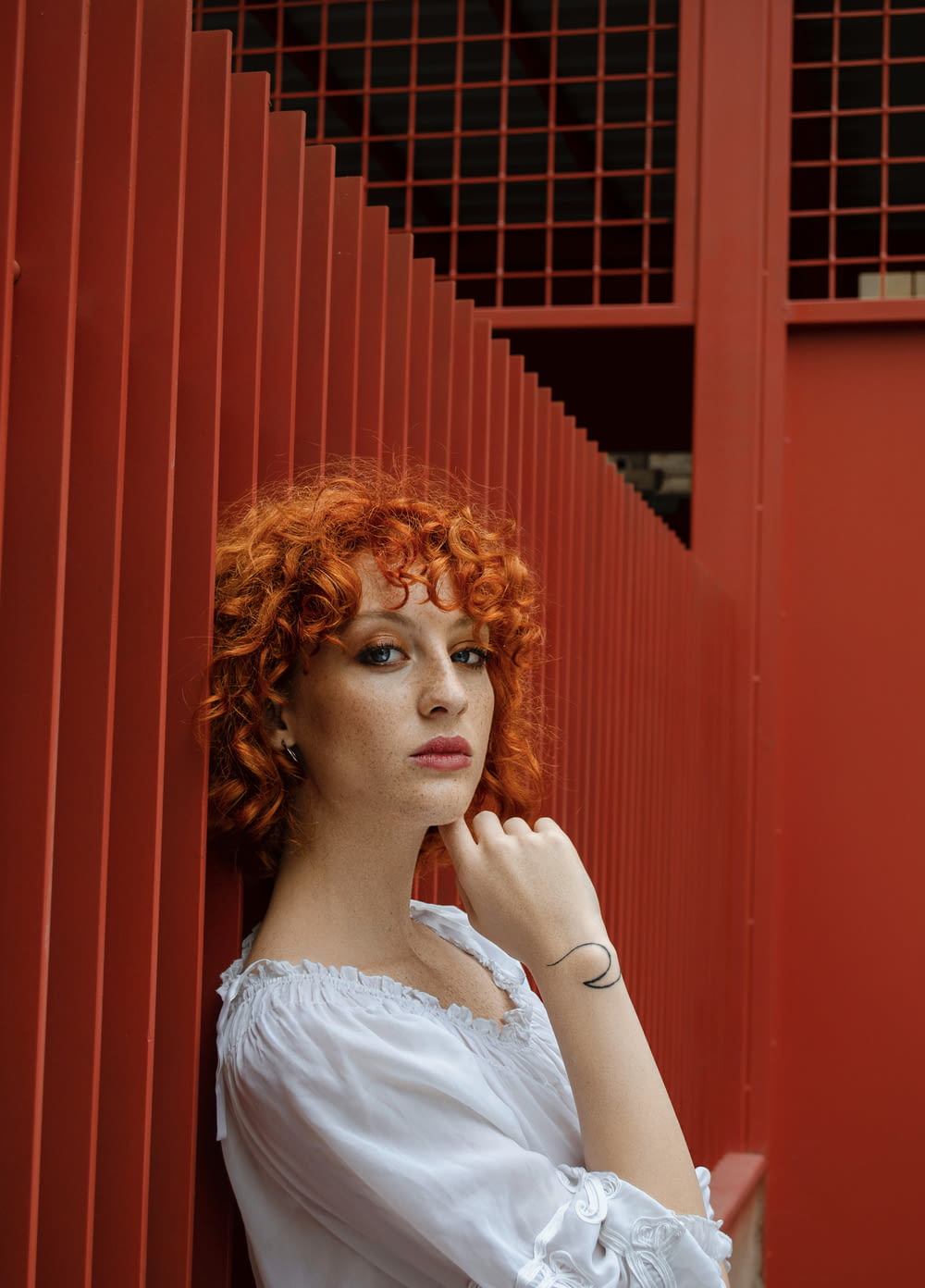 a woman with red hair leaning against a red wall