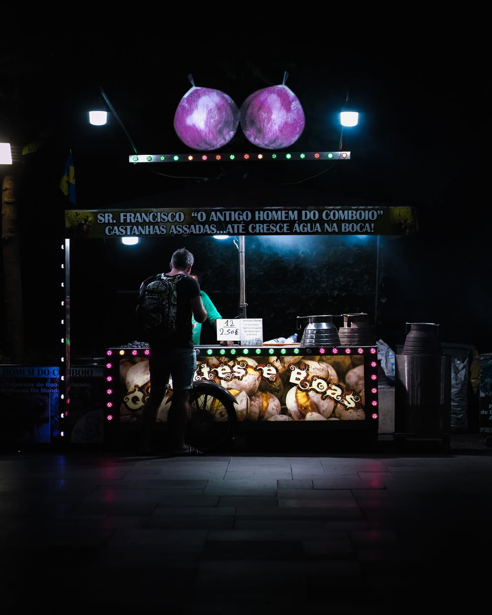 a man standing in front of a food stand at night