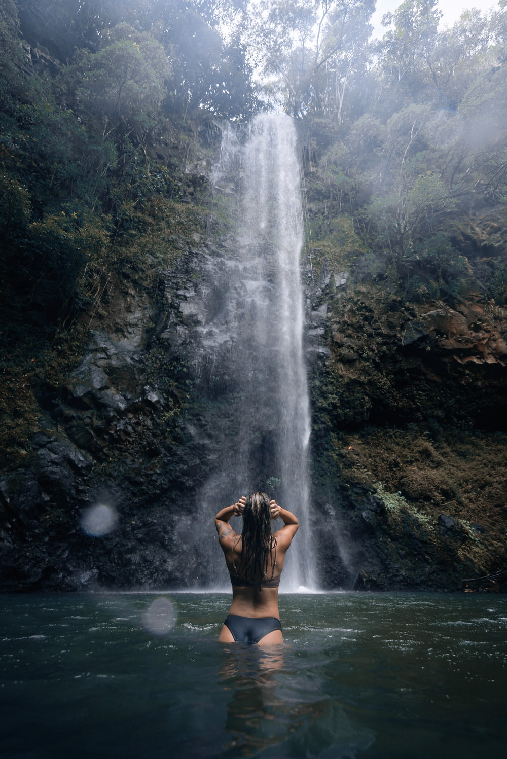 a woman standing in the water in front of a waterfall