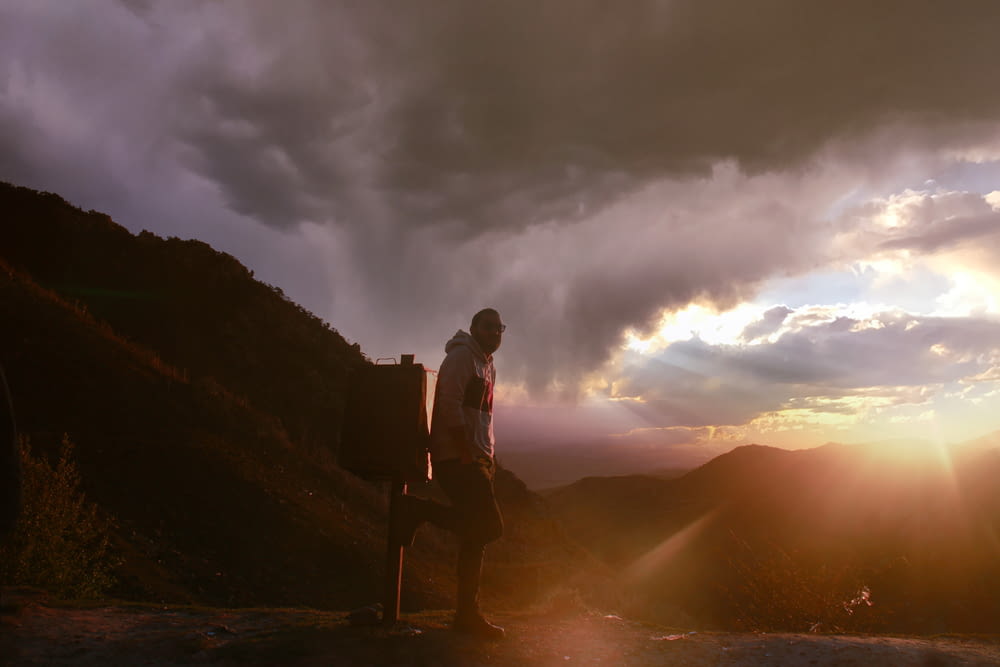 a man standing on top of a mountain under a cloudy sky