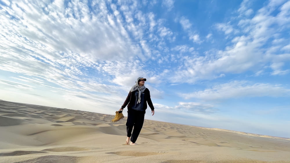 a man walking across a sandy beach under a blue sky