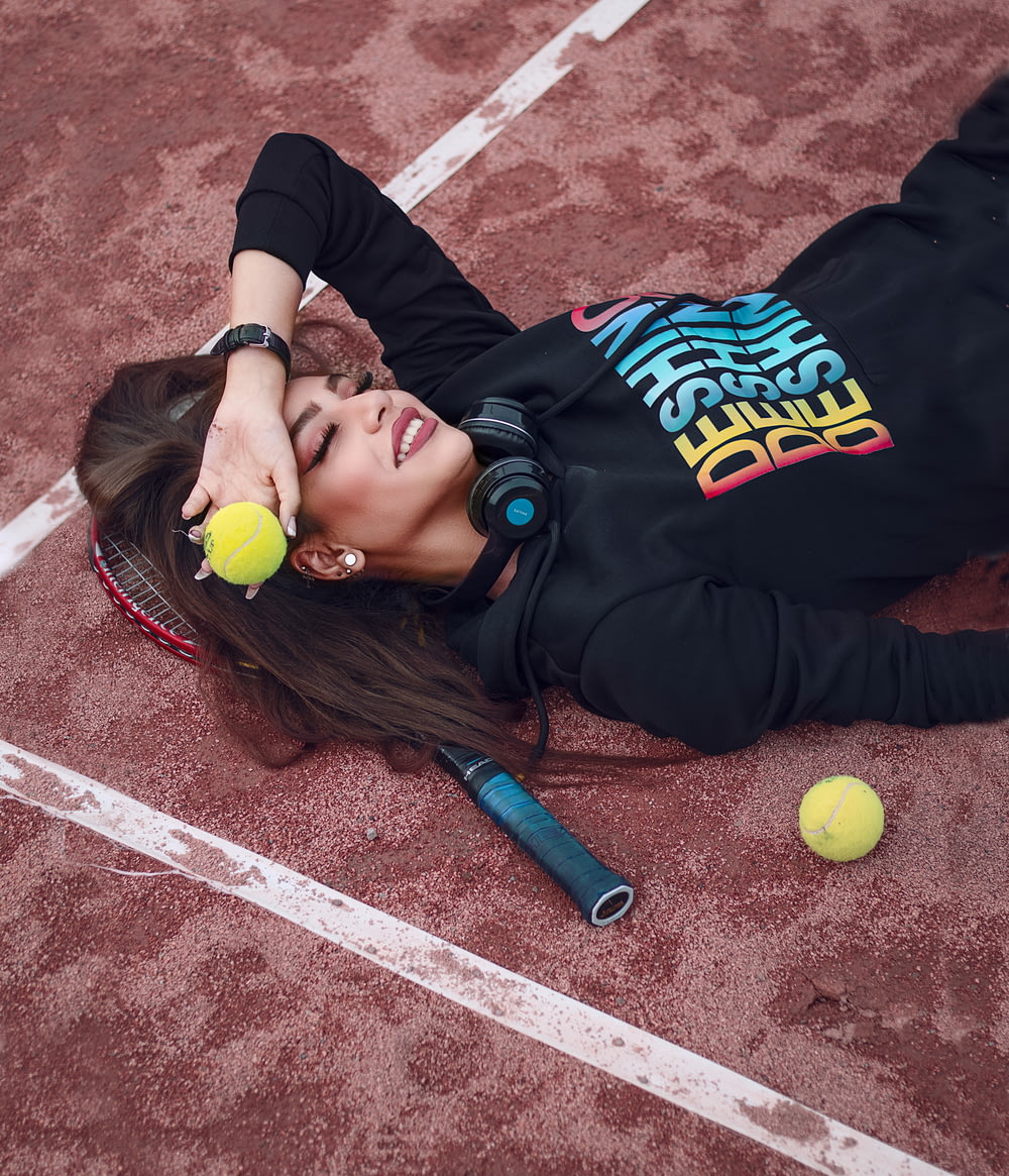 a woman laying on the ground with a tennis racket and ball