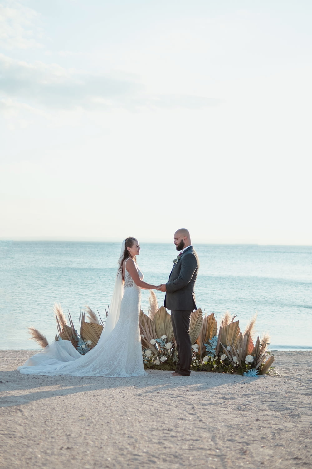 a bride and groom standing on a beach holding hands