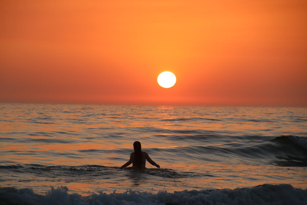 a person sitting on a surfboard in the ocean at sunset