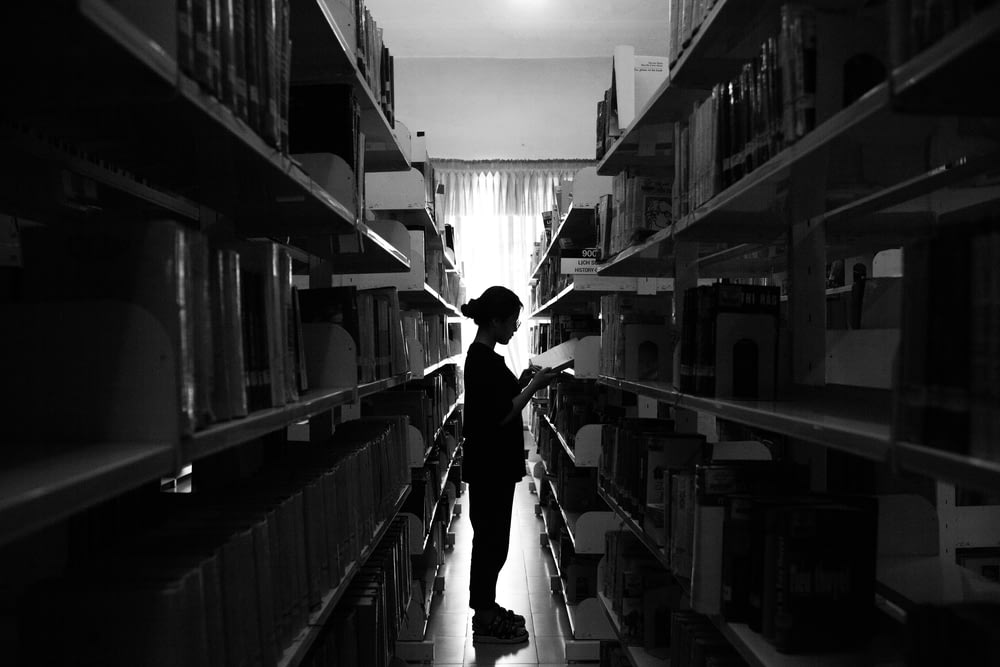 una persona de pie en una biblioteca con estantes llenos de libros
