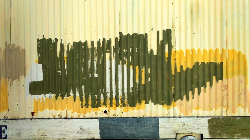 uma parede de metal enferrujada com tinta amarela e verde