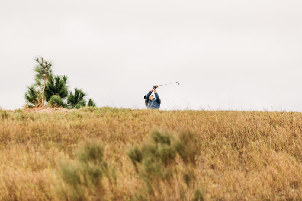 a man swinging a golf club on top of a grass covered hill