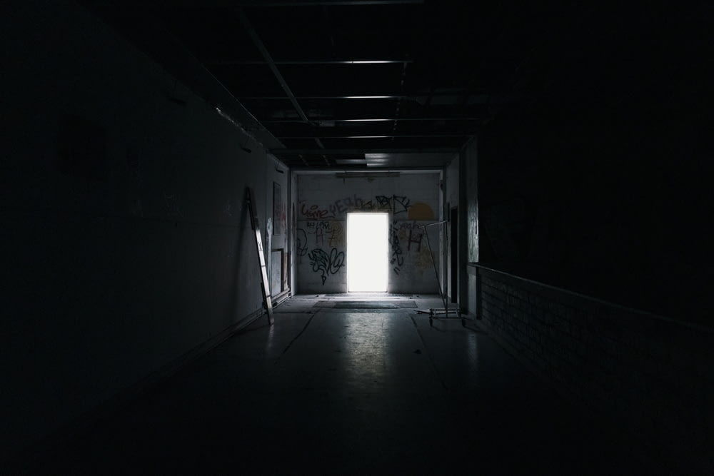 a dark hallway with a door and graffiti on the walls