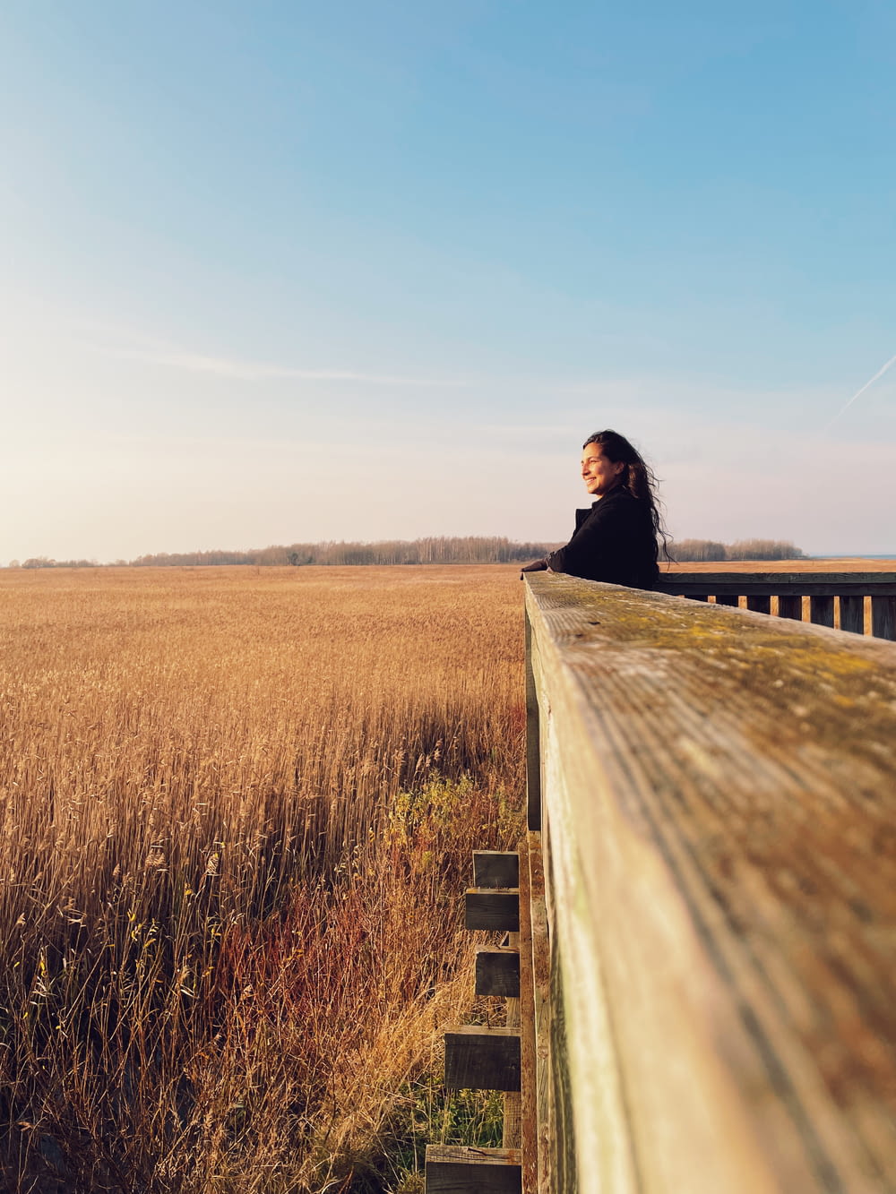 a woman sitting on a wooden bench next to a field