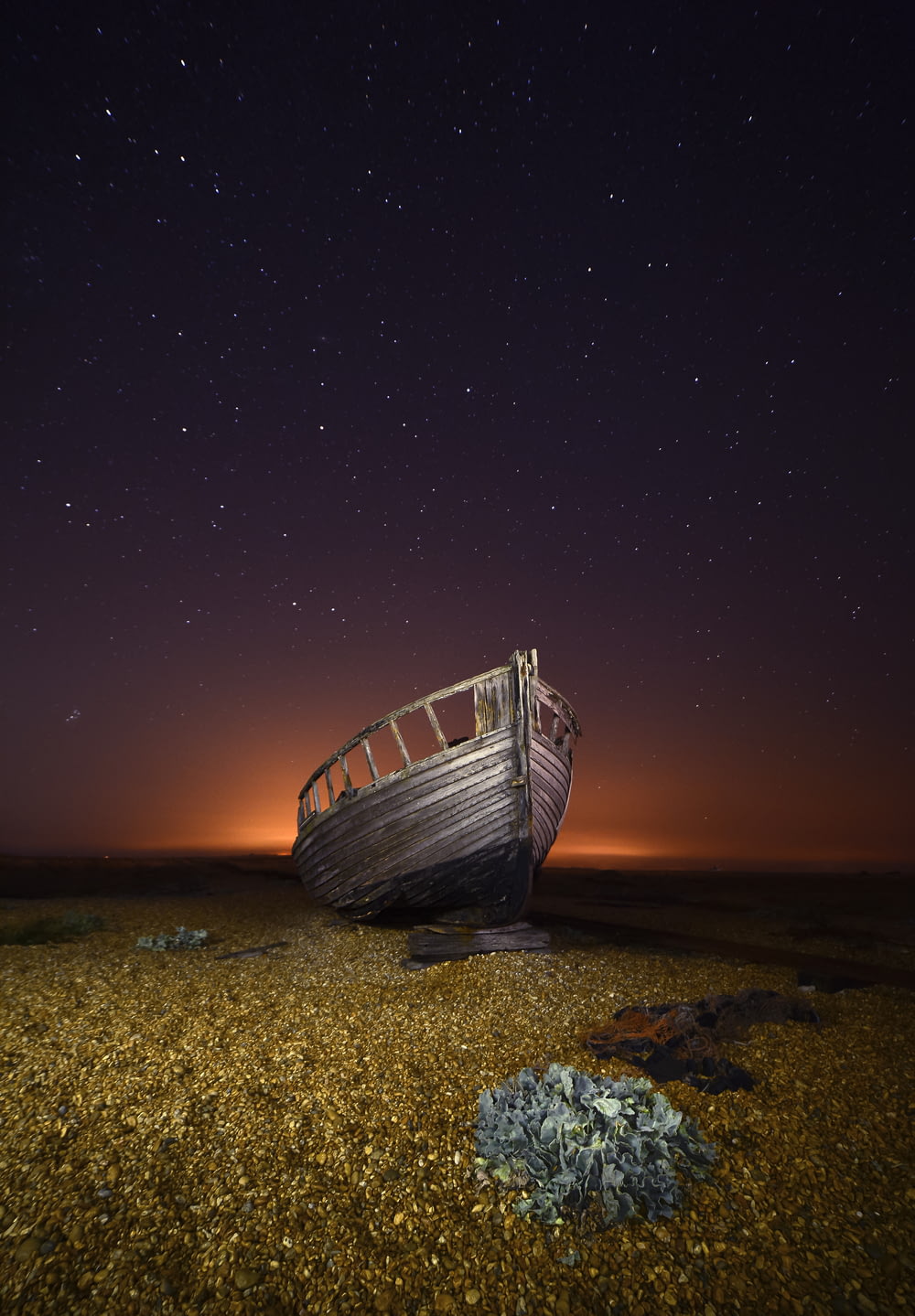 a boat sitting on top of a sandy beach under a night sky