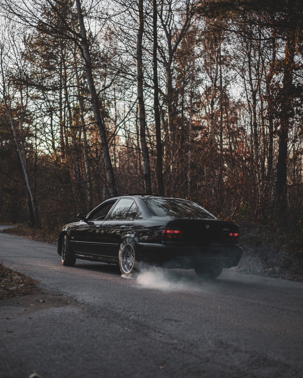 a black car driving down a road next to a forest