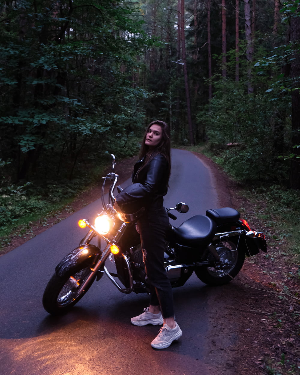 a woman standing next to a motorcycle on a road
