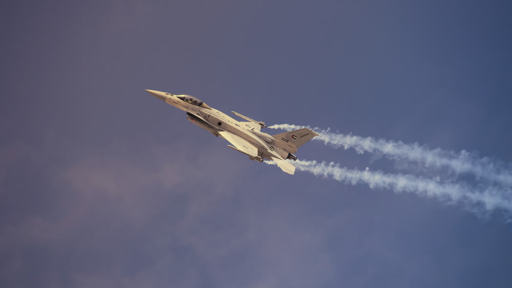 a fighter jet flying through a cloudy blue sky