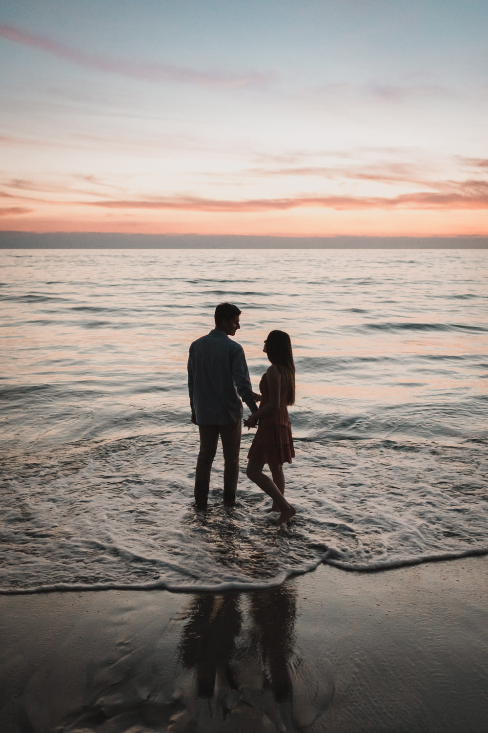 a man and a woman standing in the ocean at sunset