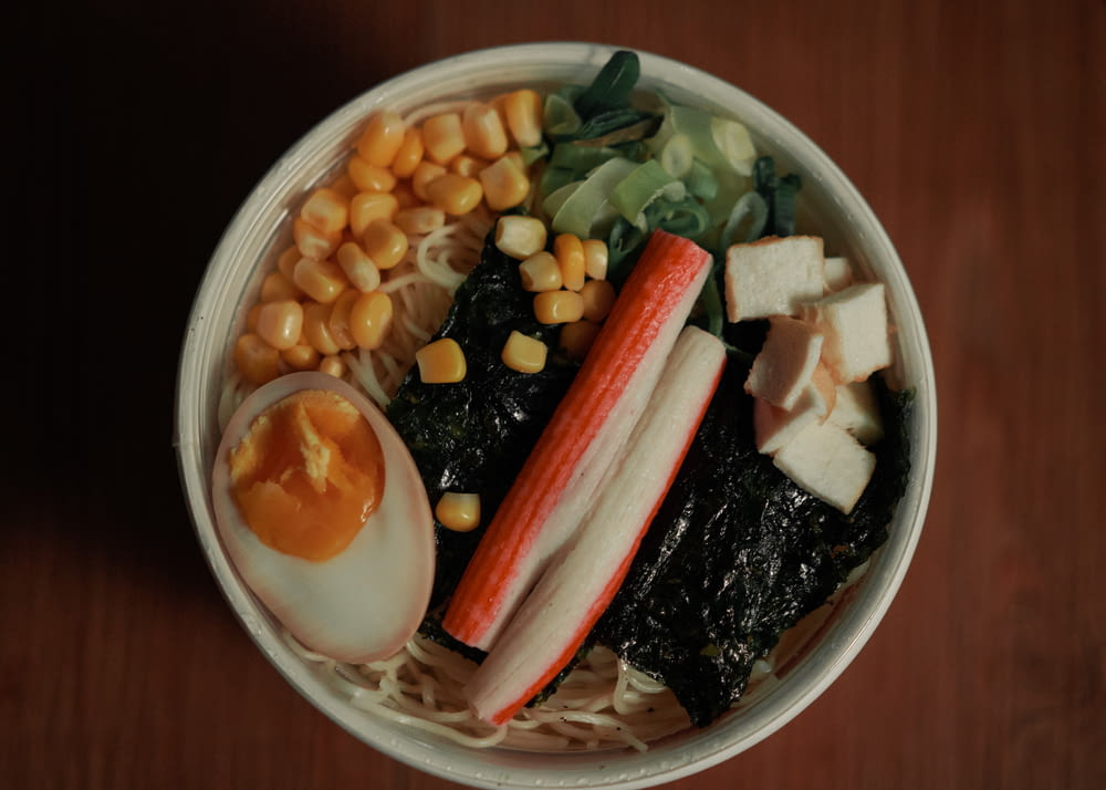 a bowl of noodles, carrots, corn, and an egg