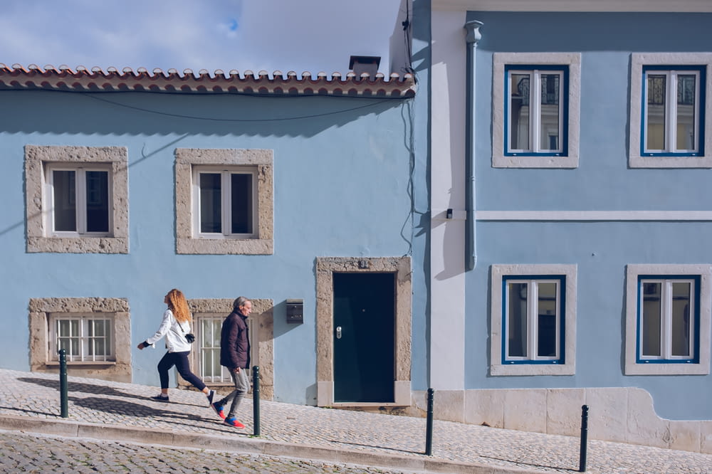 a couple of women walking down a street next to a blue building