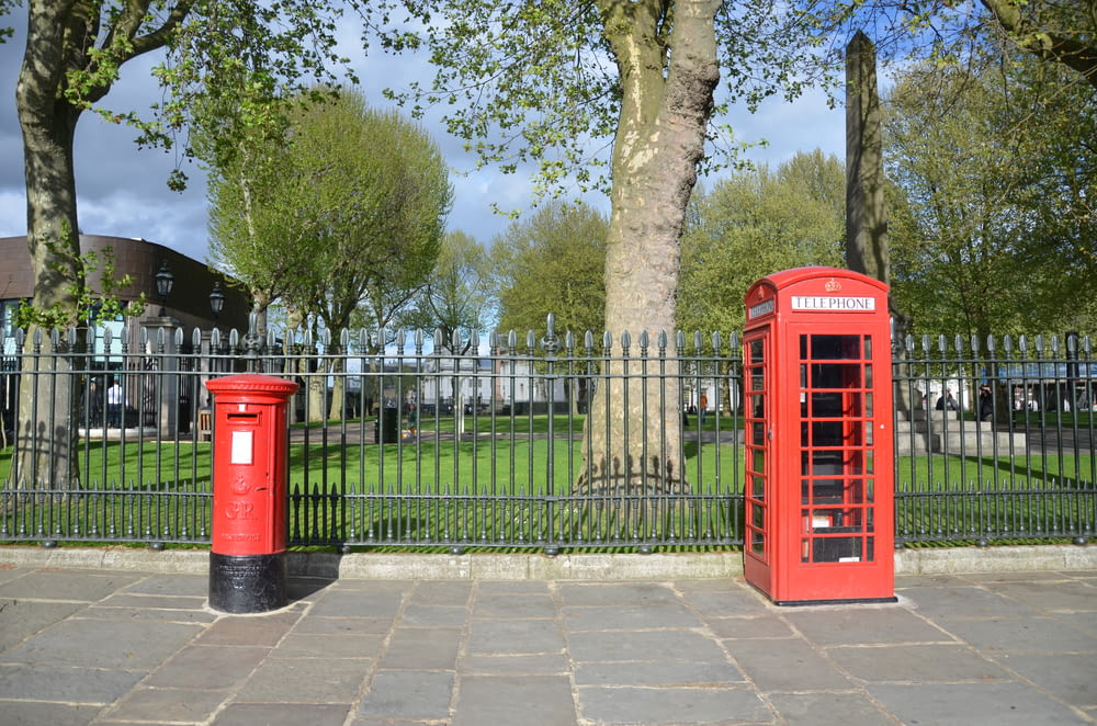 a couple of red telephone booths sitting next to a tree