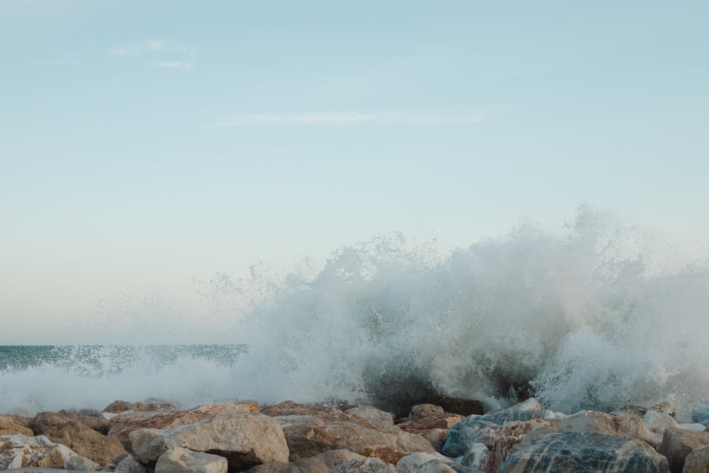 a large wave crashing over rocks on the beach