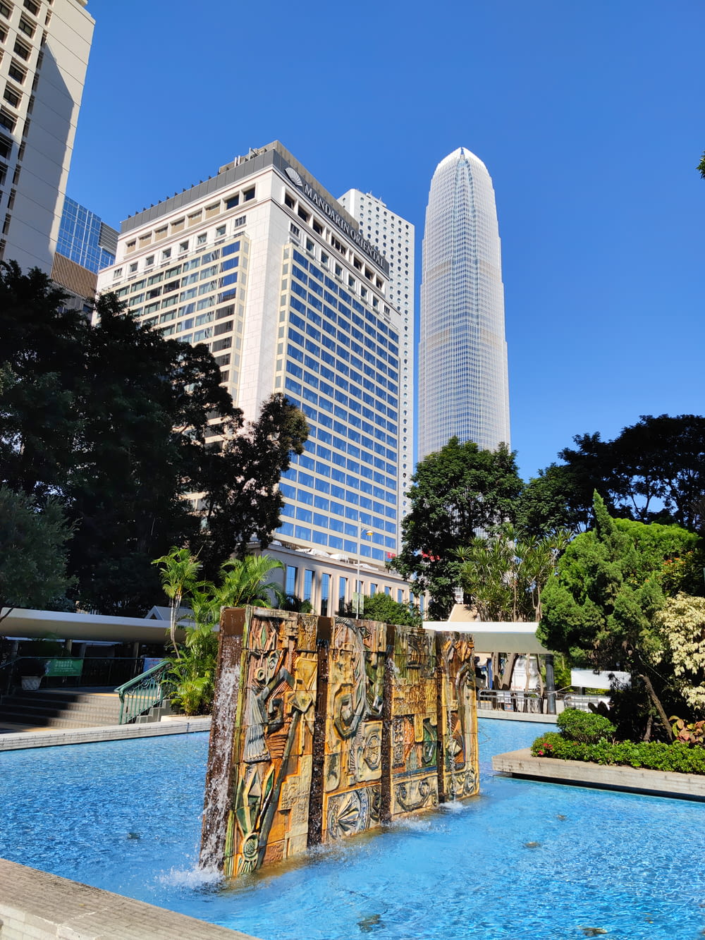 a fountain in the middle of a park with tall buildings in the background