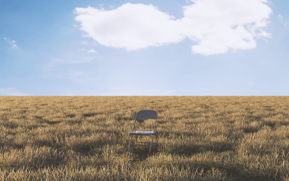 a lone chair sitting in a field of tall grass