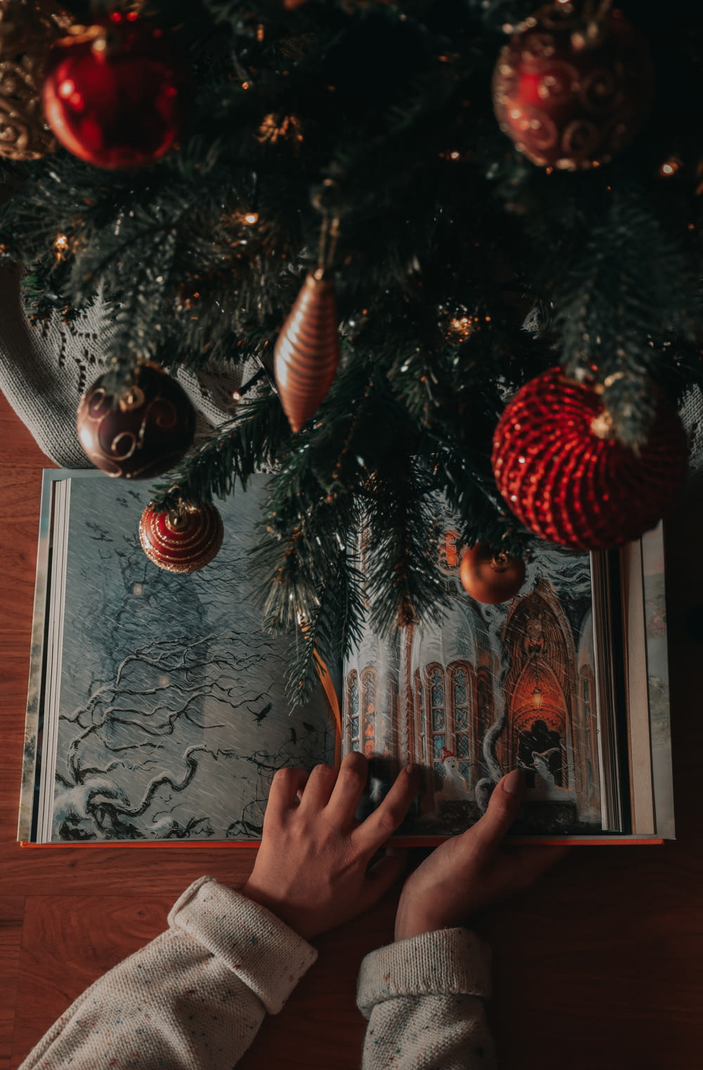 a person is reading a book under a christmas tree
