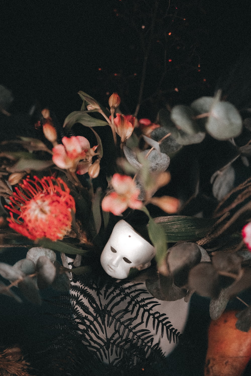 a white mask surrounded by flowers and leaves