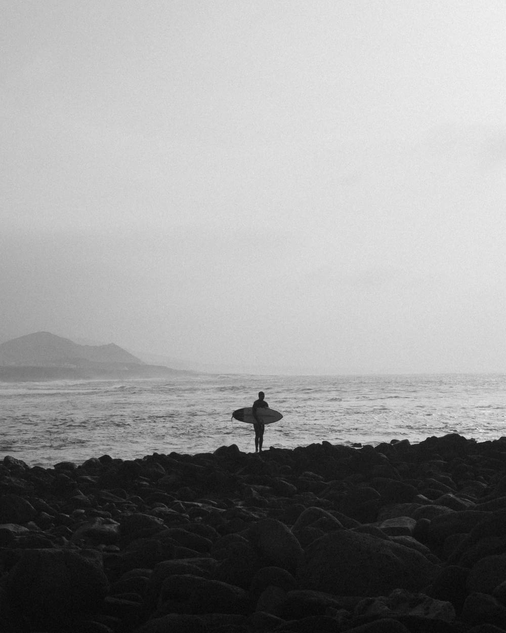 a person holding a surfboard on a rocky beach