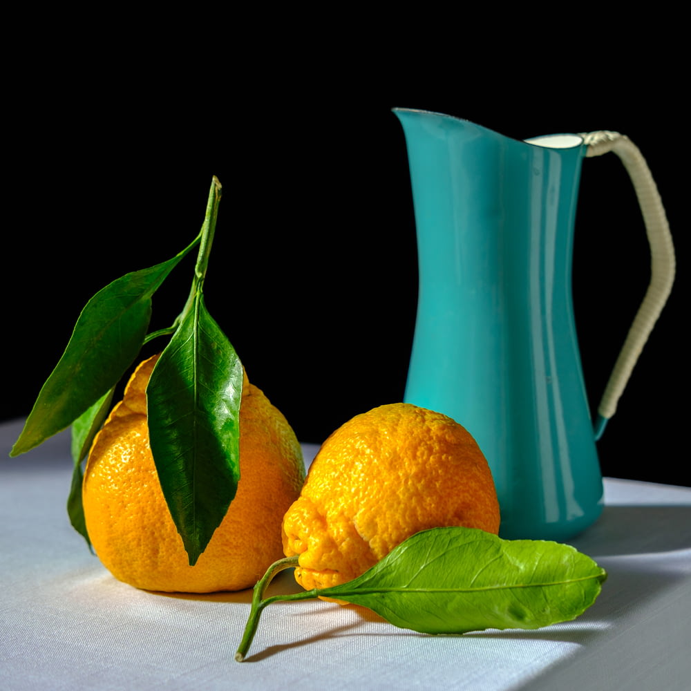 two oranges and a blue pitcher on a table