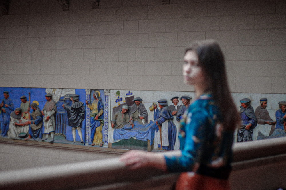 a woman standing in front of a wall with paintings on it