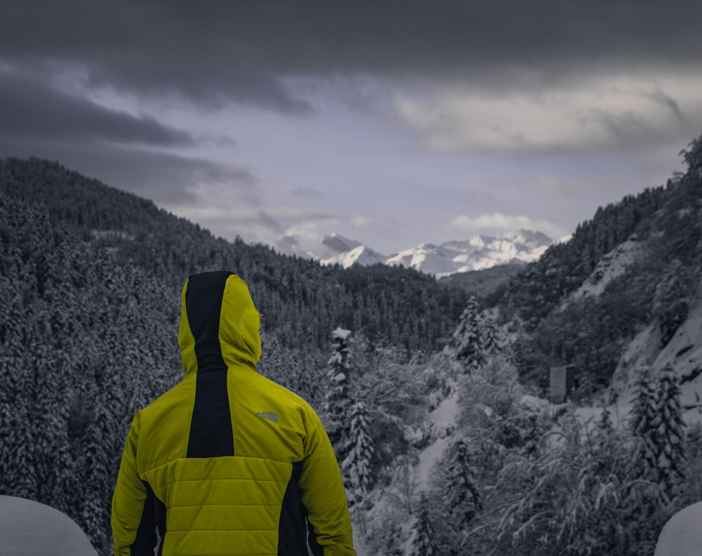 a man in a yellow jacket looking at a snowy mountain