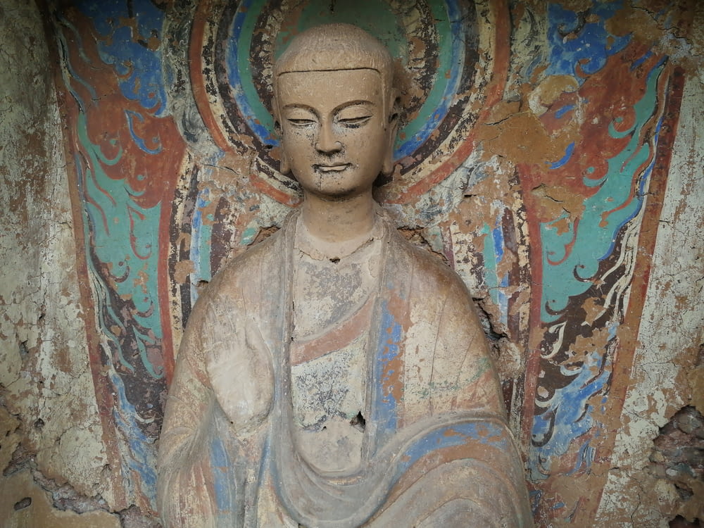 a buddha statue sitting in front of a colorful wall