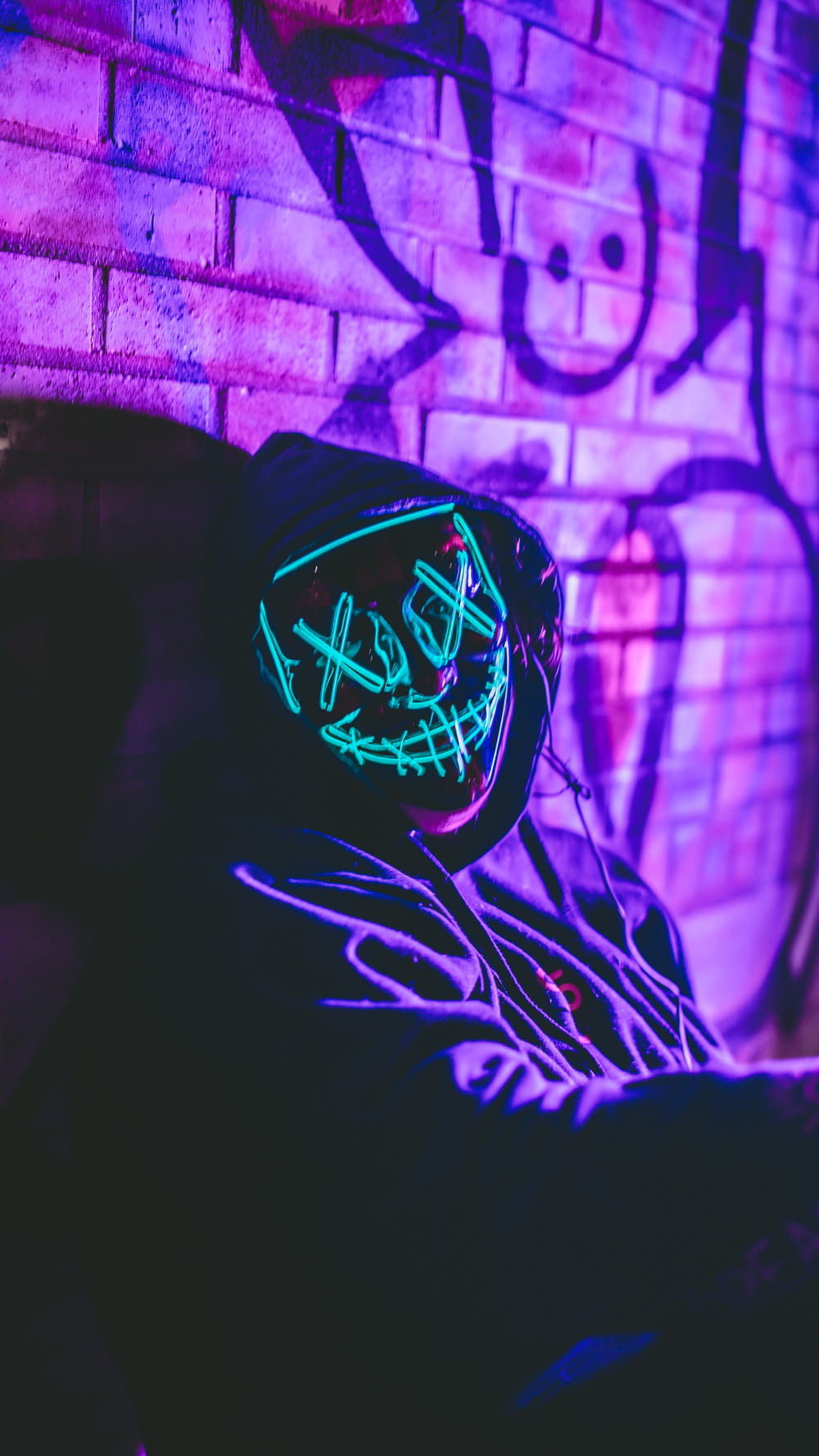 a person with a neon mask on sitting in front of a brick wall