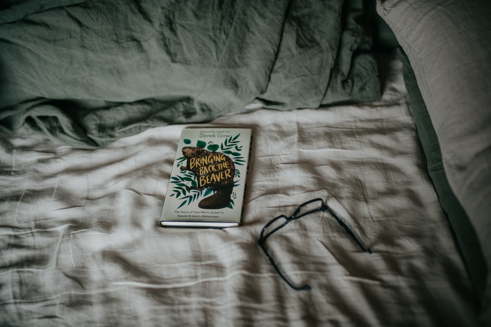 Un libro sentado encima de una cama junto a un par de gafas