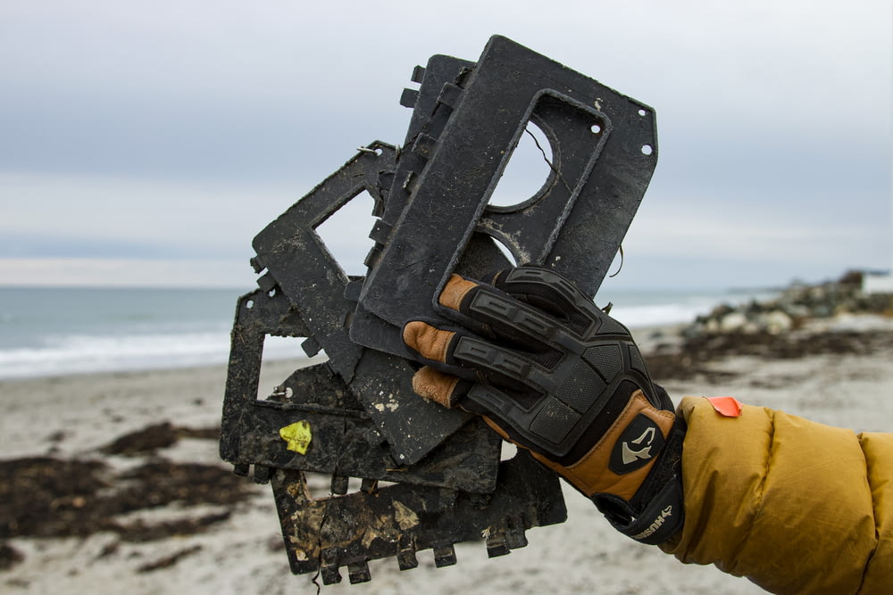 a gloved hand holding a piece of metal on a beach