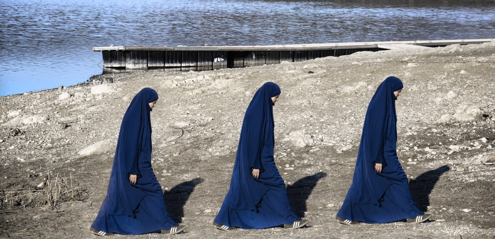 a group of women in blue veils standing in front of a body of water