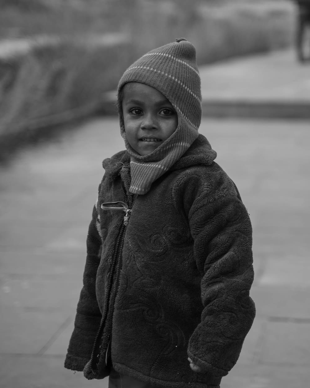 a little boy standing on a sidewalk wearing a hat