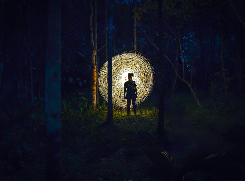 una persona in piedi nel mezzo di una foresta di notte