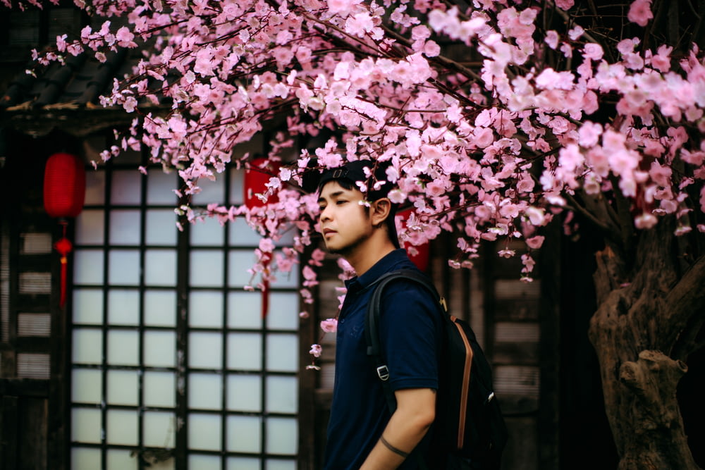 um homem de pé sob uma árvore com flores cor-de-rosa