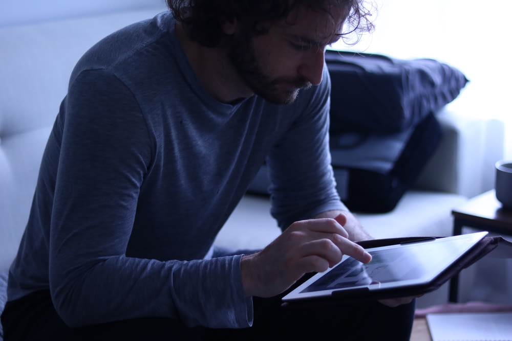 a man sitting on a couch looking at a tablet