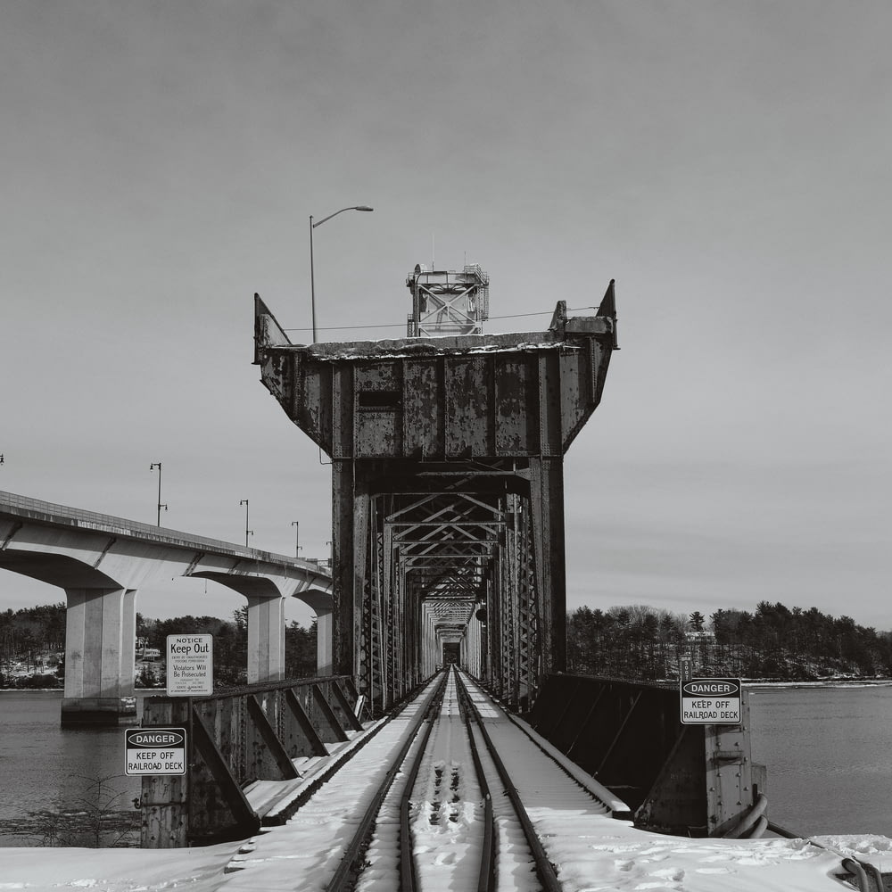uma foto em preto e branco de um trilho de trem passando por baixo de uma ponte