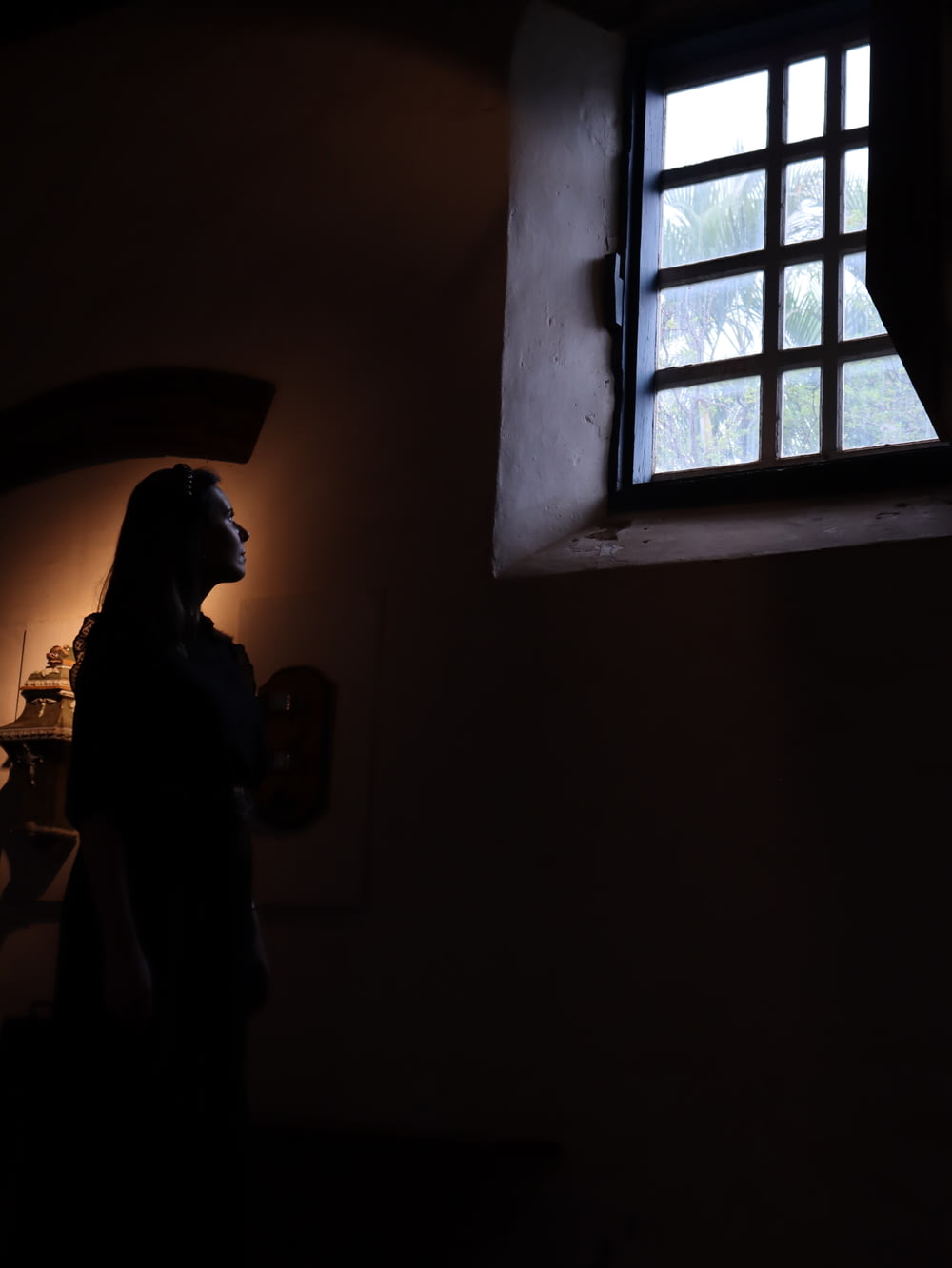 Una mujer parada frente a una ventana en una habitación oscura