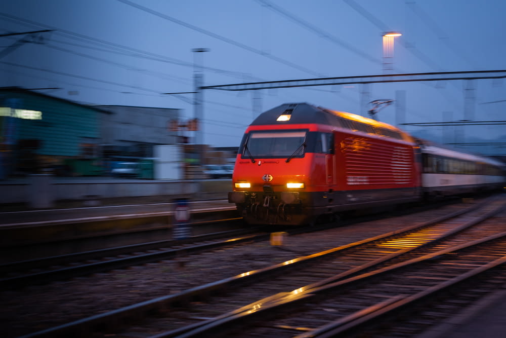 a red train traveling down train tracks next to a building