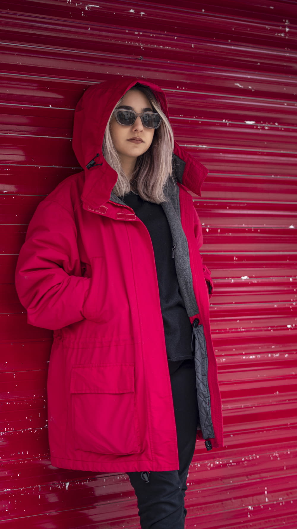 a woman in a red jacket leaning against a red wall