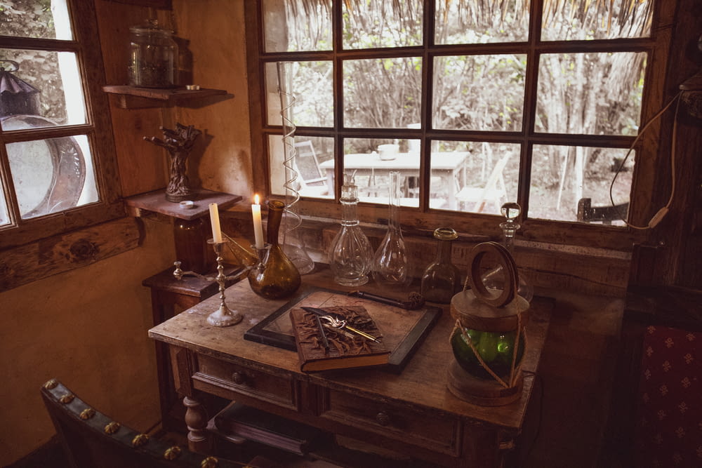 a wooden table topped with a bottle of wine next to a window