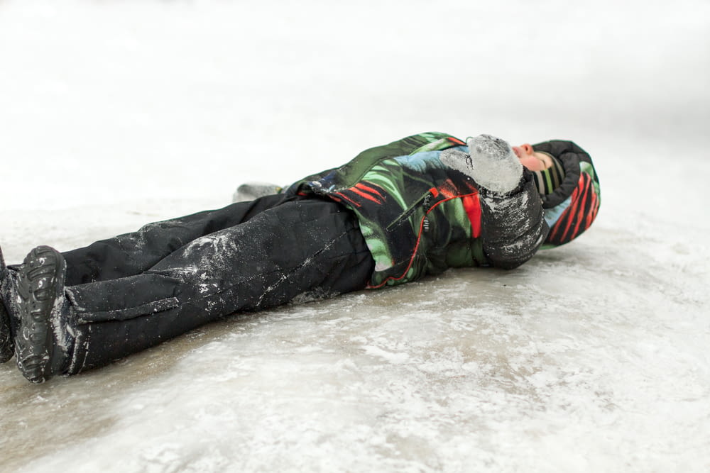 a young boy laying on the ice on a cold day