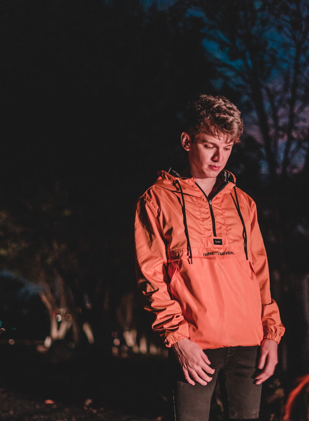 a young man standing in the dark wearing an orange hoodie
