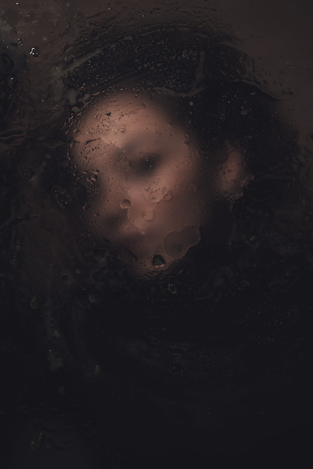 o rosto de uma mulher é visto através de uma janela coberta de chuva