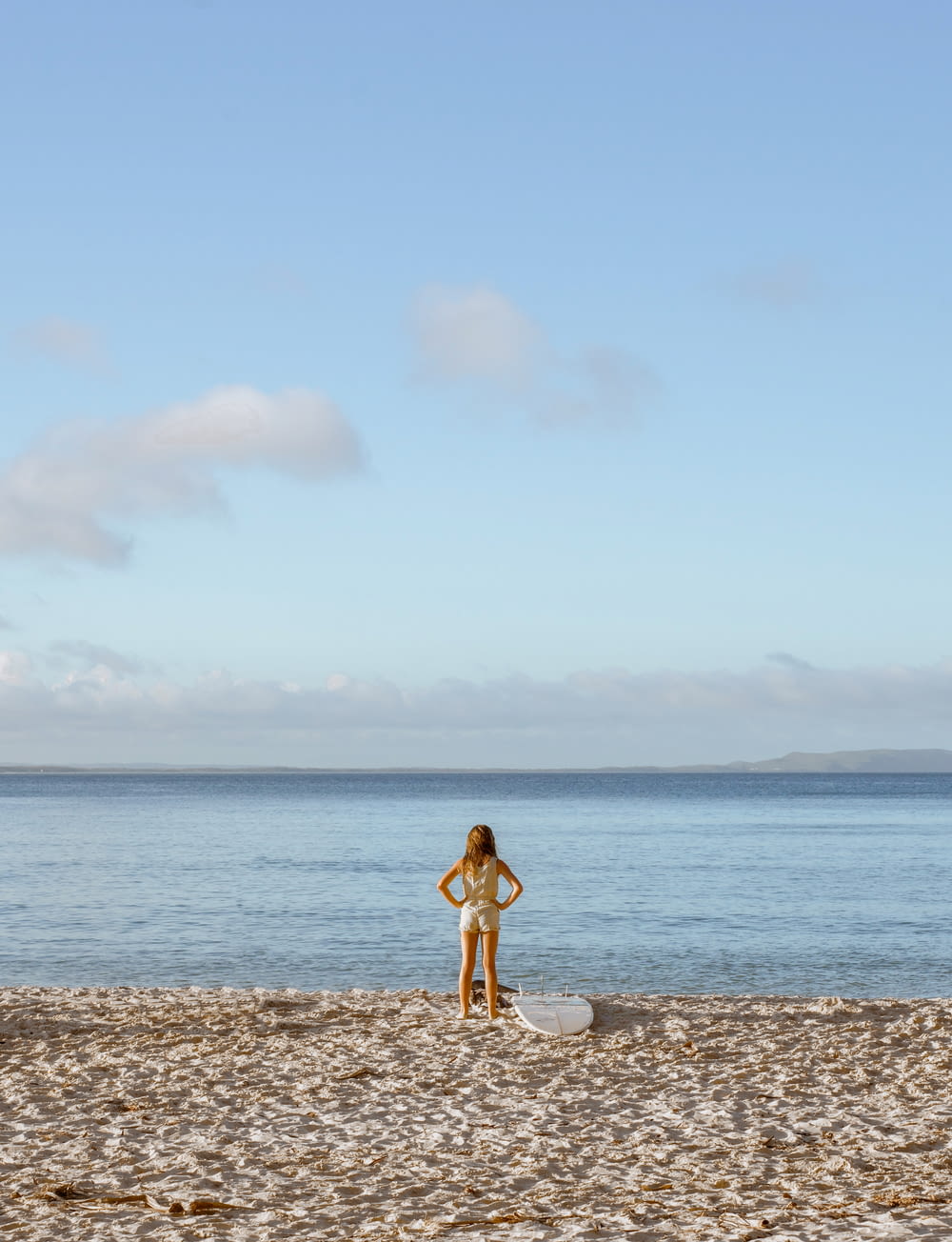サーフボードの隣のビーチに立つ女性