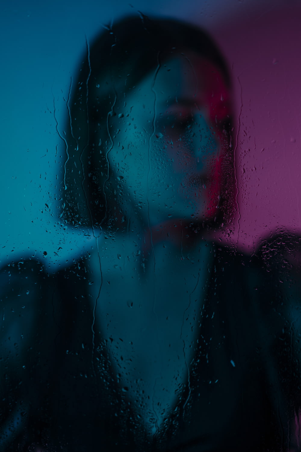 a woman standing in front of a window covered in rain